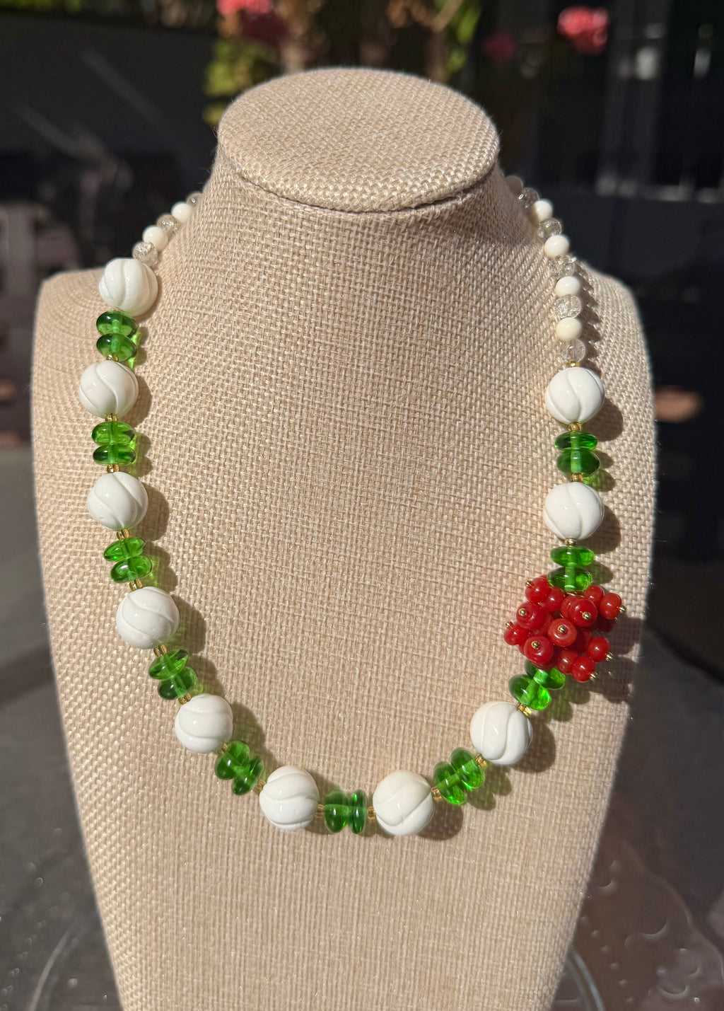 Hand-carved white shell and green glass necklace displayed on a beige fabric mannequin bust, featuring a striking red agate flower cluster side accent.