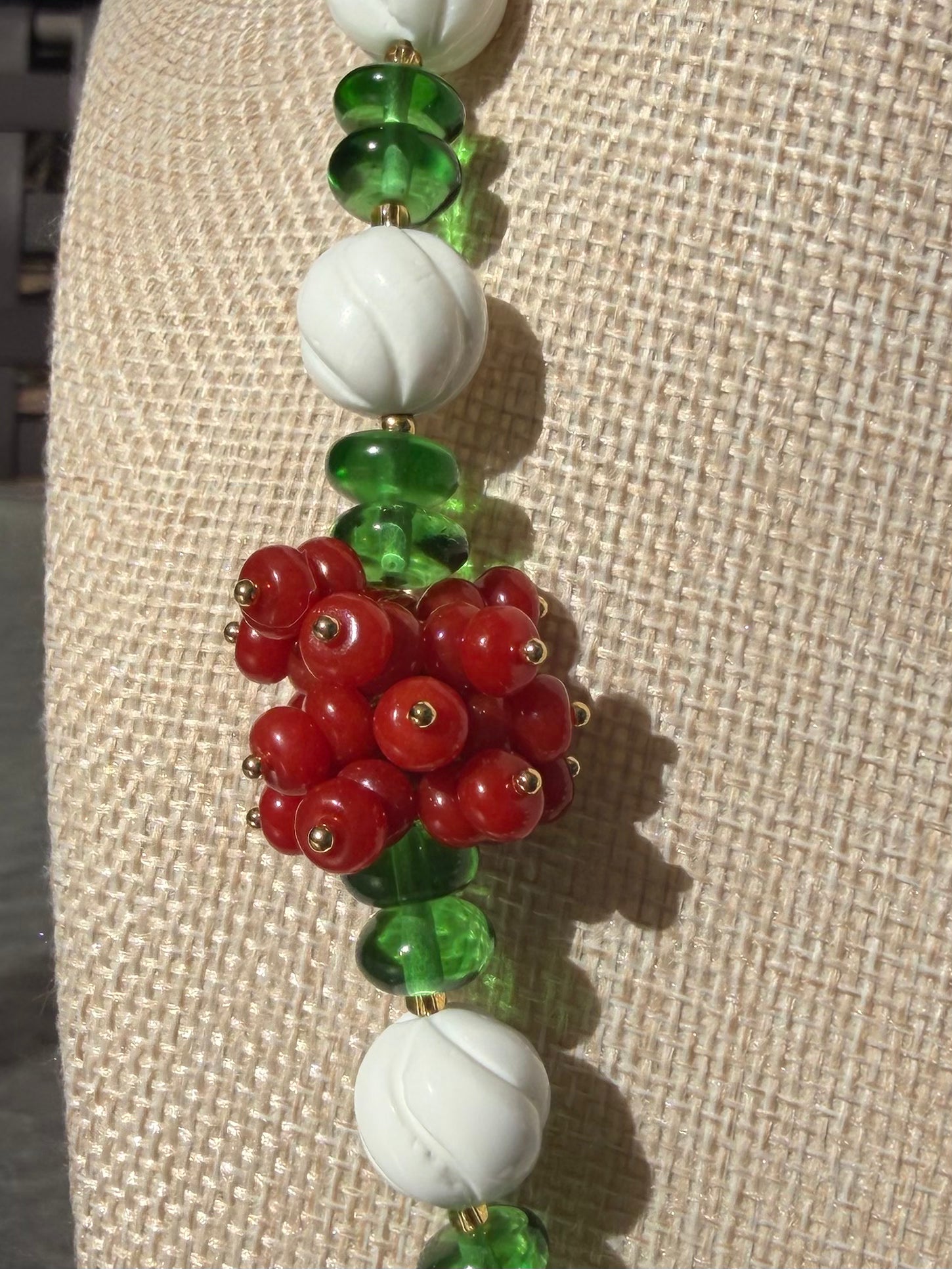 Macro close-up shot of the vibrant red Southern Red Agate flower cluster, translucent green wheel glass beads, and white spiral carved shell beads.
