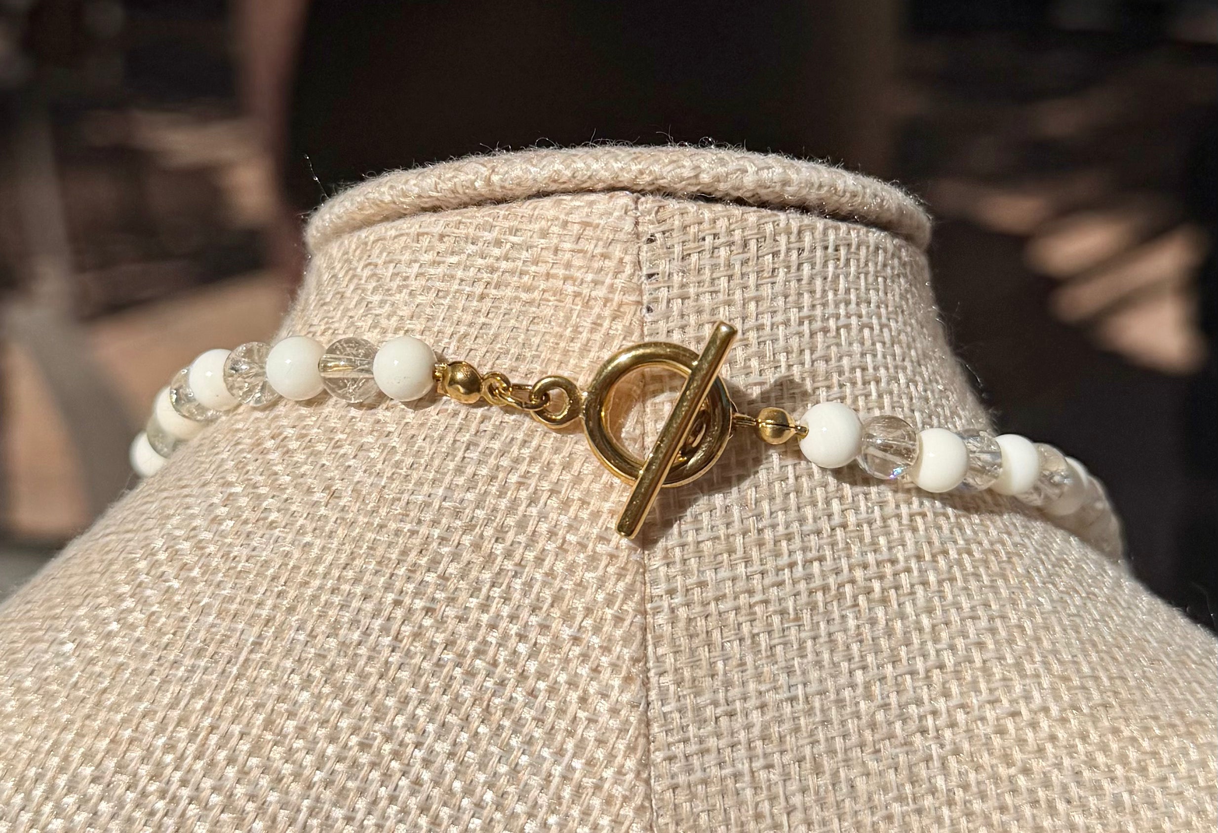 Close-up view of the gold-tone spring ring wheel clasp and delicate crystal accent beads at the back of the handcrafted shell necklace.