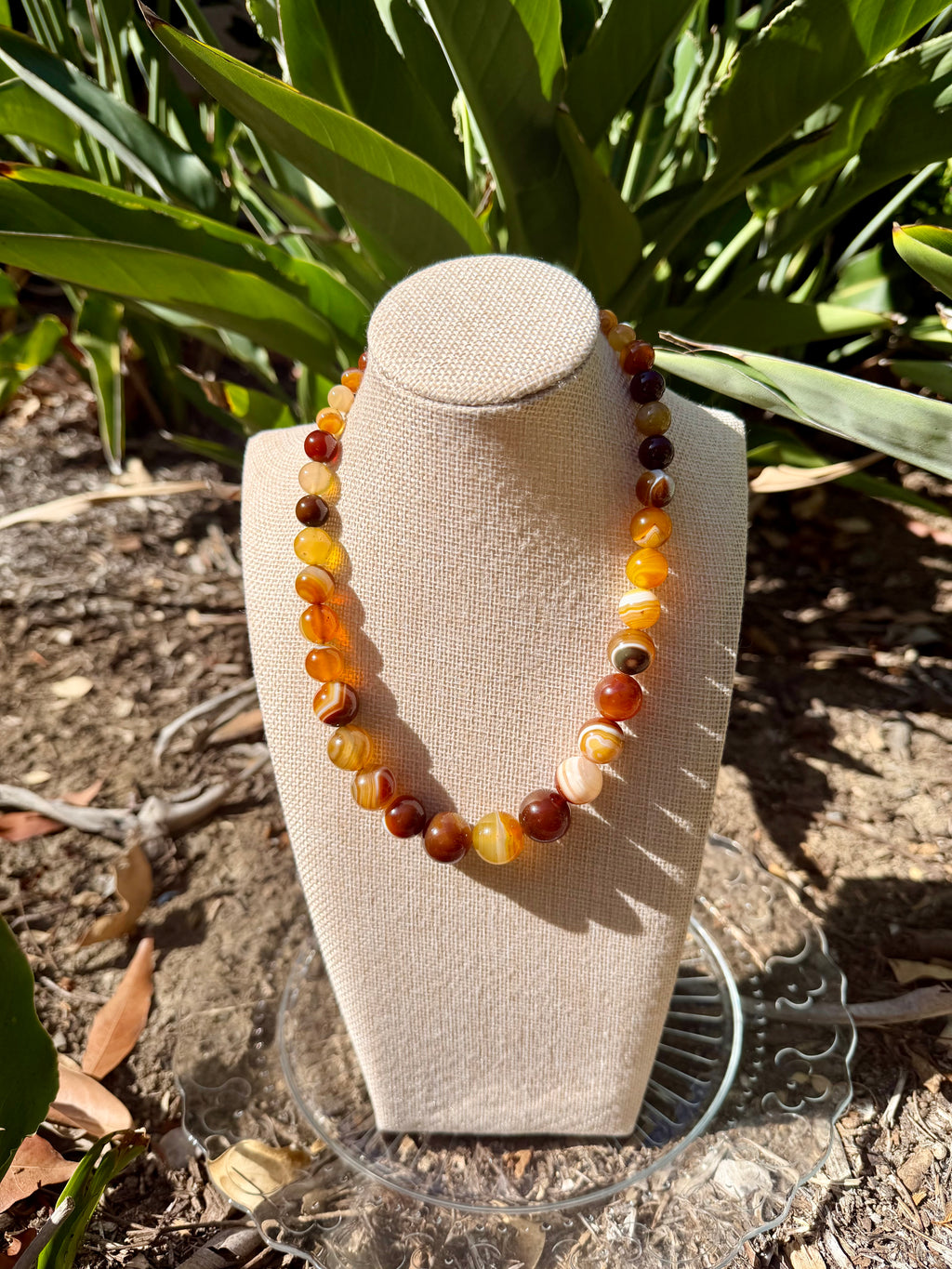 Natural banded agate tower necklace displayed on a beige fabric mannequin bust, highlighting its elegant drape and graduating brown and amber bead colors.