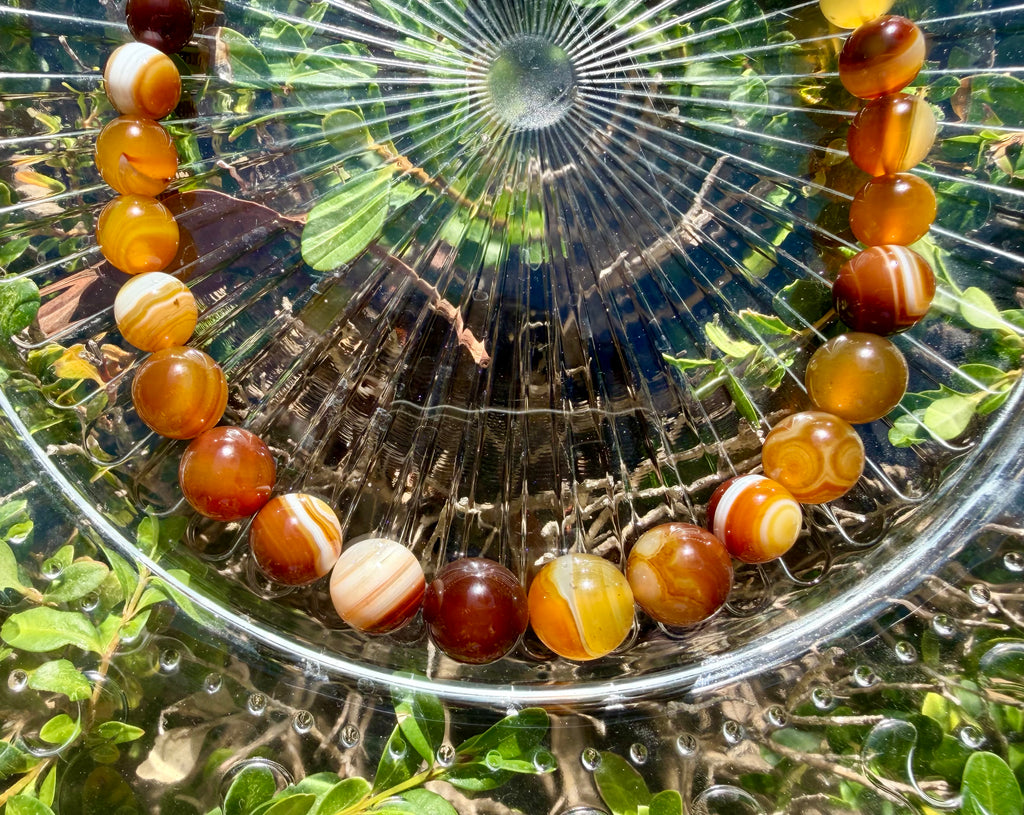 Close-up shot of the large center banded agate beads, showcasing rich natural white stripes, concentric eye patterns, and warm amber tones under sunlight.